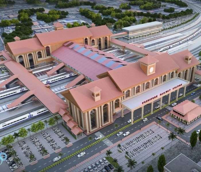 Aerial visualisation of the redeveloped Kozhikode Railway Station: the terracotta-roofed terminal building over the platforms, with large at-grade car parks and a dense two-wheeler yard filling the forecourt land around it